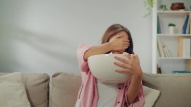 Koltukta oturan, patlamış mısır yiyen ve korku filmi izleyen genç bir kadın. Korkmuş kadın yüzünü eliyle kapatıyor. Film Türleri ve Duygusal Tepkiler.