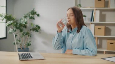 Bayan ofis çalışanı bir bardak temiz su içer. Gülümseyen bir kadın, Temiz Mineral Doğal Suyu İçen Bir Bardak Tutarak Sağlıklı Bir Yaşam Alışkanlığı ile Yeni Bir Güne Başlar. Yaşam Tarzı Sağlık Konsepti.
