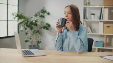Birlikte çalışmada kahve molası veren gülümseyen kadın ofis çalışanı. Dizüstü bilgisayarda çalışırken bir fincan çay içen rahat genç kadın. Günlük Rutin Konsept.