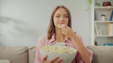 Koltukta oturan, patlamış mısır yiyen ve televizyon izleyen mutlu bir genç kadın. Neşeli Kadın Komik Bir Film İzlerken Güler. Bir Rahatlama ve Psikolojik Rahatlama Biçimi olarak filmler. Çevrimiçi Sinema.