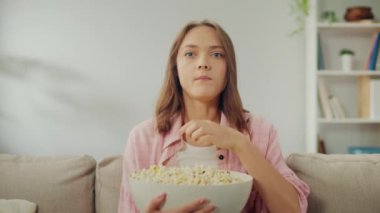 Koltukta oturan, patlamış mısır yiyen ve televizyon izleyen mutlu bir genç kadın. Neşeli Kadın Komik Bir Film İzlerken Güler. Bir Rahatlama ve Psikolojik Rahatlama Biçimi olarak filmler. Çevrimiçi Sinema.