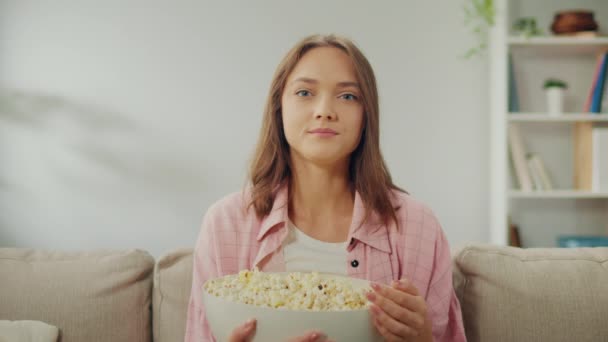 Μια Χαρούμενη Νεαρή Γυναίκα Κάθεται Στον Καναπέ Τρώει Ποπ Κορν — Αρχείο Βίντεο