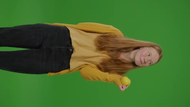 绿色屏风 垂直录像 少女一边吃苹果一边笑着 象征着一个苹果 健康饮食和学校营养 青春在日常饮食中拥抱营养选择的生动描写 — 图库视频影像