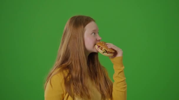 绿色屏风 年轻迷人的女孩喜欢吃美味的大汉堡 现代社会健康选择与快餐诱惑的反差 反式脂肪 脂肪食物 — 图库视频影像