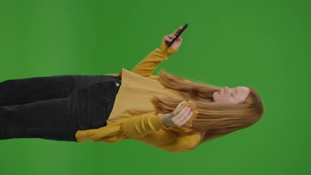 Függőleges Videó Zöld Vászon Lány Böngészi Mobilját Miközben Egy Hamburgert — Stock videók