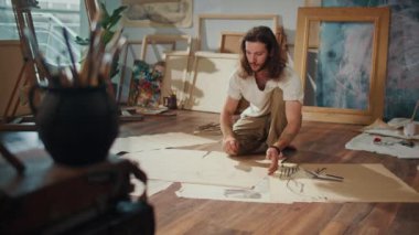 Genç Bir Sanatçı Samimi Stüdyosunda Yerde Boya Yapıyor, Etrafı Bitirdiği Çalışmalarla çevrili. Parlak, Yaratıcı Uzay, ona yeni, eşsiz sanat eserlerini sıcak ve davetkar bir ortamda yaratması için ilham veriyor..