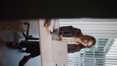 Dikey video. Bir İş Kadını Modern Ofiste Geç Saatlere Kadar Çalışıyor, Pozitif Atmosferi Koruyor ve İş-Yaşam Dengesi İçin Çabalıyor. Akşam Verimliliği, Teşvik Edici Çevre.