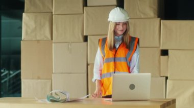 Hard Hat 'teki Kadın Mühendis ve Yüksek Görünebilirlik Yeleği Dizüstü bilgisayarındaki Planları Gözden geçirirken Gülümsüyor. Endüstriyel Ekipmanlarla çevrelenmiş durumda, Profesyonelliği, İnşaattaki Güvenliği temsil ediyor..