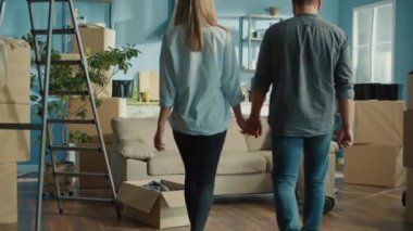 Bir çift, taşınma kutularıyla çevrili yeni dairelerinde el ele yürüyorlar. Bu an, İlk Paylaştıkları Evlerinde Birlikte Yeni Bir Bölüm Başlarken Mutluluklarını ve Heyecanlarını Yakalıyor