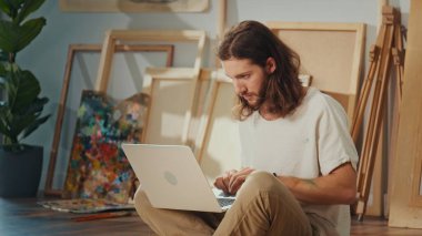 Artist Paints on the Floor in His Cozy, Bright Studio, Surrounded by His Completed Works. The Light-Filled, Inspiring Environment Encourages Him to Create New, Unique Pieces of Art in a Relaxing Space clipart