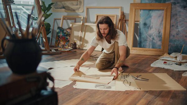 A Young Artist Paints on the Floor in His Cozy Studio, Surrounded by His Finished Works. The Bright, Creative Space Inspires Him to Create New, Unique Pieces of Art in a Warm and Inviting Environment.