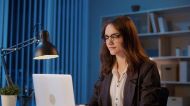 Genç Bir Kadın Ofis İşçisi Akşam Ofisinde Oturuyor, Geç Saatlere Kadar Çalışıyor ve Profesyonel Yorgunlukla Mücadele Ediyor Ve Ofis Yorgunluğu İyileşme Gereğini ve Uzun Saatlerin Gerilimini Vurguluyor