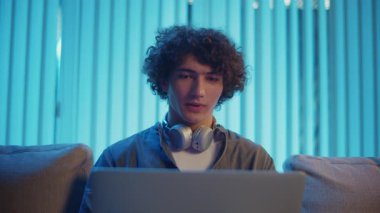 Uzaktan Çalışma, Dijital İletişim, Odaklanma Modu. Genç Adam geceleri koltukta dizüstü bilgisayarla Kucak 'ta oturur, Online bir toplantıya katılır. Melez Yaşam Tarzında Sıradan Ama Üretken Bir Akşam