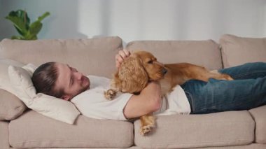 Yavaş Yaşam, Akıl Sağlığı, Hayvan Rahatlığı. Adam kanepeye uzanmış köpeğiyle dinleniyor. Basit, Duygusal Bağlanma, Varlık ve Evde Sakinlik Anı