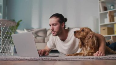 Mikro neşeler, Akıl Sağlığı, Günlük Denge. Genç Adam, köpeği ile koltukta iletişim kurarken dizüstü bilgisayarda çalışıyor. Yumuşak, destekleyici bir an Harmanlayıcı Odak, Duygu ve Bağlantı