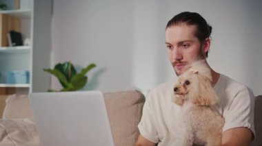 Duygusal Destek, Akıl Sağlığı, İş-Yaşam Dengesi. Evden Genç Adam Çalışıyor, Köpeği Yanında Otururken Çevrimiçi Toplantıya Odaklanıyor. Dijital Bağlantının Sakin Anı ve Hayvan güdümlü İstikrar