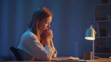 Yumuşak Gece Işığının Altında İncil okuyan Genç Kadın Elleri Duayla Katlandı. Sakin İnanç Anı, Ruhsal Yansıma, Vahiy Arayışı, Derin Barış ve Tanrı 'yla İç Bağlantı.