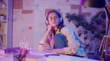 Gen Z Yaşam Tarzı, Dijital Çoklu Görev, Neon Mood. Genç Kız Müzik Dinlerken ve Dizüstü bilgisayar izlerken resim çizer. Neon Işığında Modern Gençliğin Yaratıcı Kaosu 'nda Kişisel İfade