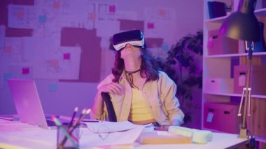 Karışık Gerçeklik, Enmersive Tech, Gen Z Future. Neon-Lit Room 'da oturan kız VR ya da AR gözlükleri takıyor, Dijital Alanla etkileşimde. Görsel olarak Yoğun Sanal Dünya Kişisel Anı