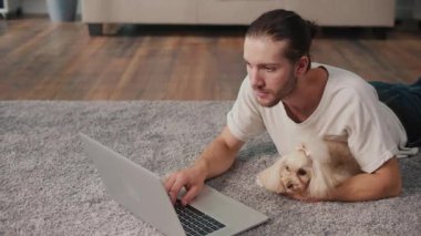 İş-Hayat Bütünleşmesi, Odaklanmış Rutin. Dikey video. Genç adam, köpeğiyle birlikte evde dizüstü bilgisayarda çalışıyor. Sakin Duygusal İstikrar, Rahatlık ve Her Gün Hayvanlara Özel Verimlilik Sahnesi