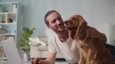 Mikro neşeler, Akıl Sağlığı, Günlük Denge. Genç Adam, köpeği ile koltukta iletişim kurarken dizüstü bilgisayarda çalışıyor. Yumuşak, destekleyici bir an Harmanlayıcı Odak, Duygu ve Bağlantı