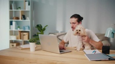 Mikro neşeler, Akıl Sağlığı, Günlük Denge. Genç Adam, köpeği ile koltukta iletişim kurarken dizüstü bilgisayarda çalışıyor. Yumuşak, destekleyici bir an Harmanlayıcı Odak, Duygu ve Bağlantı
