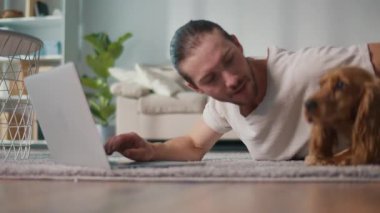 Mikro neşeler, Akıl Sağlığı, Günlük Denge. Genç Adam, köpeği ile koltukta iletişim kurarken dizüstü bilgisayarda çalışıyor. Yumuşak, destekleyici bir an Harmanlayıcı Odak, Duygu ve Bağlantı