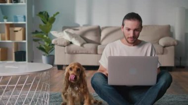 Mikro neşeler, Akıl Sağlığı, Günlük Denge. Genç Adam, köpeği ile koltukta iletişim kurarken dizüstü bilgisayarda çalışıyor. Yumuşak, destekleyici bir an Harmanlayıcı Odak, Duygu ve Bağlantı