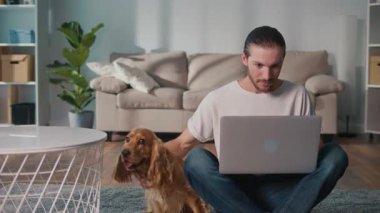 Mikro neşeler, Akıl Sağlığı, Günlük Denge. Genç Adam, köpeği ile koltukta iletişim kurarken dizüstü bilgisayarda çalışıyor. Yumuşak, destekleyici bir an Harmanlayıcı Odak, Duygu ve Bağlantı