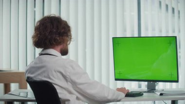 Modern Şehir Ofisinde oturan bir doktor yeşil ekranlı bir bilgisayar üzerinde çalışıyor. Yüksek kalite tıbbi hizmetler sunuyor, hızlı yaşam tarzlarına terzilik hizmeti veriyor. Sağlık hizmetleri kavramı