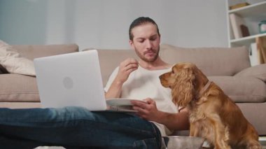 Sağlıklı rutin, Evcil Hayvan Besleme, Dijital Denge. Köpeği yakınlarda kendi yemeğinin tadını çıkarırken adam masa başında çalışıyor ve yiyor. Sakin, Senkronize Sağlık ve Günlük Odaklanma