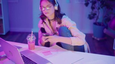 Gen Z Yaşam Tarzı, Dijital Çoklu Görev, Neon Mood. Genç Kız Müzik Dinlerken ve Dizüstü bilgisayar izlerken resim çizer. Neon Işığında Modern Gençliğin Yaratıcı Kaosu 'nda Kişisel İfade