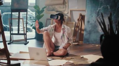 Bir Kadın Sanatçı Parlak Stüdyosunda Eşsiz Sanatlar Yaratmak İçin VR Gözlük Kullanıyor, Bitirdiği Çalışmalarla Çevrelenmiş Video, Geleneksel Resim ve 3 boyutlu Sanat Yaratmak için VR Teknolojisinin Harmanını Vurguluyor