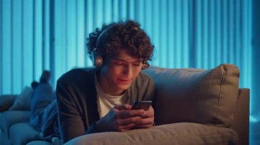 Man, Kanepe Kaydırma Telefonunda Rahatlıyor, Muhtemelen Podcast veya Browsing dinliyor. Günlük Kişisel Bakım ve Dijital Çağ 'da Yavaş Yaşam. Dijital Detox, Akıl Sağlığı, Odaklanma Kipi.