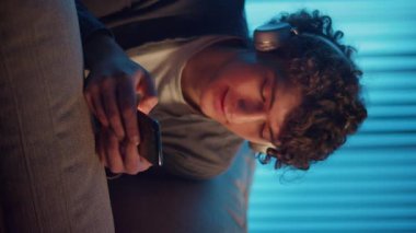 Man, Kanepe Kaydırma Telefonunda Rahatlıyor, Muhtemelen Podcast veya Browsing dinliyor. Günlük Kişisel Bakım ve Dijital Çağ 'da Yavaş Yaşam. Dikey Video, Dijital Detox, Ruh Sağlığı, Odaklanma Kipi.