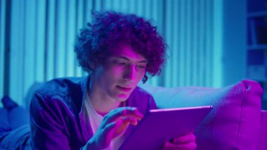 Man, Tablet Kullanarak Koltuğa Rahatlar, Muhtemelen Okuma ve Yayınlama İçeriğini İzler. Günlük Kişisel Bakım ve Dijital Çağ 'da Yavaş Yaşam. Dijital Detox, Akıl Sağlığı, Odaklanma Kipi.