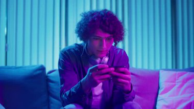 Man, Kanepe Kaydırma Telefonunda Rahatlıyor, Muhtemelen Podcast veya Browsing dinliyor. Günlük Kişisel Bakım ve Dijital Çağ 'da Yavaş Yaşam. Dijital Detox, Akıl Sağlığı, Odaklanma Kipi.