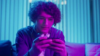 Man, Kanepe Kaydırma Telefonunda Rahatlıyor, Muhtemelen Podcast veya Browsing dinliyor. Günlük Kişisel Bakım ve Dijital Çağ 'da Yavaş Yaşam. Dijital Detox, Akıl Sağlığı, Odaklanma Kipi.