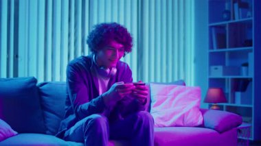 Man, Kanepe Kaydırma Telefonunda Rahatlıyor, Muhtemelen Podcast veya Browsing dinliyor. Günlük Kişisel Bakım ve Dijital Çağ 'da Yavaş Yaşam. Dijital Detox, Akıl Sağlığı, Odaklanma Kipi.