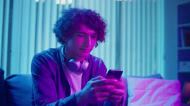 Man, Kanepe Kaydırma Telefonunda Rahatlıyor, Muhtemelen Podcast veya Browsing dinliyor. Günlük Kişisel Bakım ve Dijital Çağ 'da Yavaş Yaşam. Dijital Detox, Akıl Sağlığı, Odaklanma Kipi.