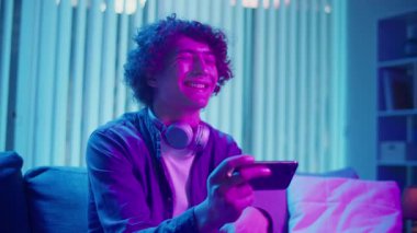 Genç adam geceleri koltukta oturur, telefon ekranına güler. Dijital Günlük Yaşamda Eğlence, Rahatlama ve Bağlanma Anı. Ruh Sağlığı, Dijital Bağlantı, Duygusal Rahatlama.