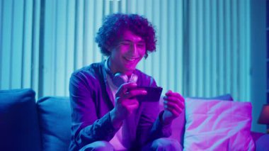 Genç adam geceleri koltukta oturur, telefon ekranına güler. Dijital Günlük Yaşamda Eğlence, Rahatlama ve Bağlanma Anı. Ruh Sağlığı, Dijital Bağlantı, Duygusal Rahatlama.