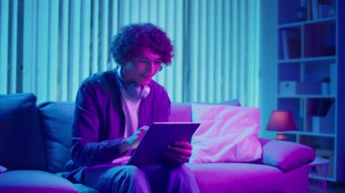 Man, Tablet Kullanarak Koltuğa Rahatlar, Muhtemelen Okuma ve Yayınlama İçeriğini İzler. Günlük Kişisel Bakım ve Dijital Çağ 'da Yavaş Yaşam. Dijital Detox, Akıl Sağlığı, Odaklanma Kipi.