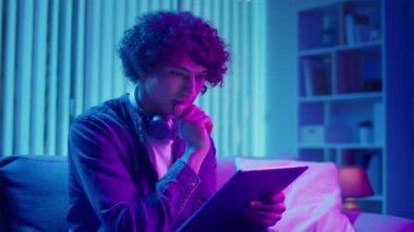 Genç adam tabletle koltukta oturuyor, konsantrasyonla çalışıyor. Esnek Teknolojik Çalışma Akışı 'nda sakin ve etkili bir akşam. Odaklanma Kipi, Dijital Üretim, Özyönetim.