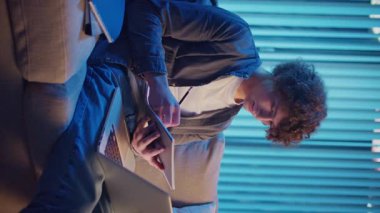 Genç Adam Neon Light 'ta, Kanepede Gece Çalışır, Not Defteri ve Laptop Tutar. Sakin Üretkenlikle Gen Z Çalışma Programı. Dikey Video, Uzaktan Öğrenme, Dijital Günlük, Estetik Odaklanma.