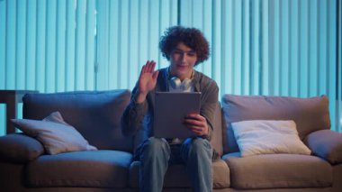 Genç Adam geceleri koltukta dizüstü bilgisayarla Kucak 'ta oturur, Online bir toplantıya katılır. Melez Yaşam Tarzında Sıradan Ama Üretken Bir Gece. Uzaktan Çalışma, Dijital İletişim, Odaklanma Kipi.