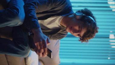 Man, Kanepe Kaydırma Telefonunda Rahatlıyor, Muhtemelen Podcast veya Browsing dinliyor. Günlük Kişisel Bakım ve Dijital Çağ 'da Yavaş Yaşam. Dikey Video, Dijital Detox, Ruh Sağlığı, Odaklanma Kipi.