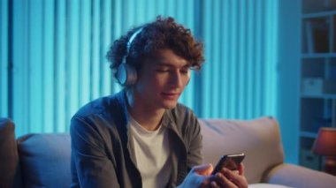 Man, Kanepe Kaydırma Telefonunda Rahatlıyor, Muhtemelen Podcast veya Browsing dinliyor. Günlük Kişisel Bakım ve Dijital Çağ 'da Yavaş Yaşam. Dijital Detox, Akıl Sağlığı, Odaklanma Kipi.