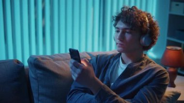 Man, Kanepe Kaydırma Telefonunda Rahatlıyor, Muhtemelen Podcast veya Browsing dinliyor. Günlük Kişisel Bakım ve Dijital Çağ 'da Yavaş Yaşam. Dijital Detox, Akıl Sağlığı, Odaklanma Kipi.