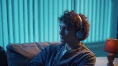 Genç adam geceleri kulaklıkla koltukta oturur, müzik dinler ve dinlenir. Duygusal Denge ve Zihinsel Refah İçin Akşam Ritüeli. Farkındalık, Ses Terapisi, Dijital Sakinlik.